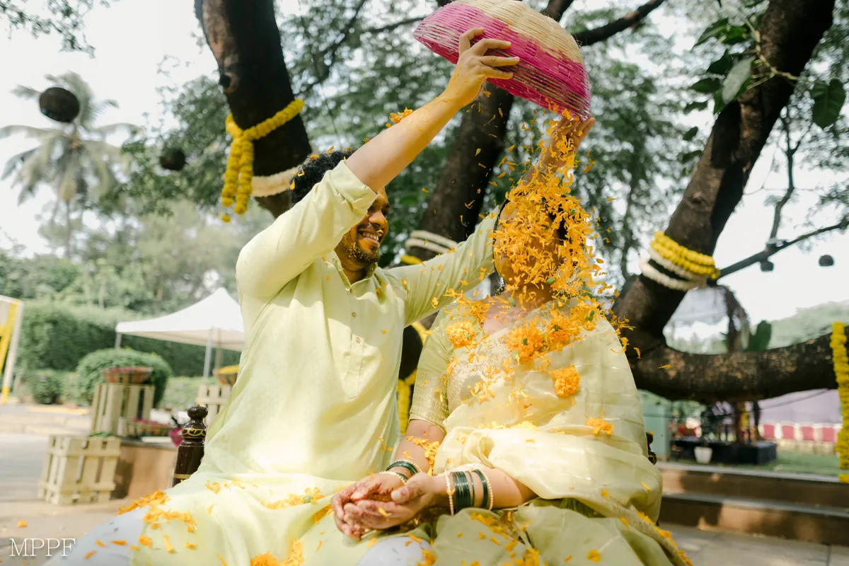 At the haldi, the groom tips a pink basket of marigold petals over the bride