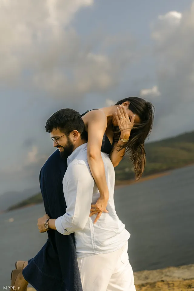 Man carrying his partner by a lake, both laughing