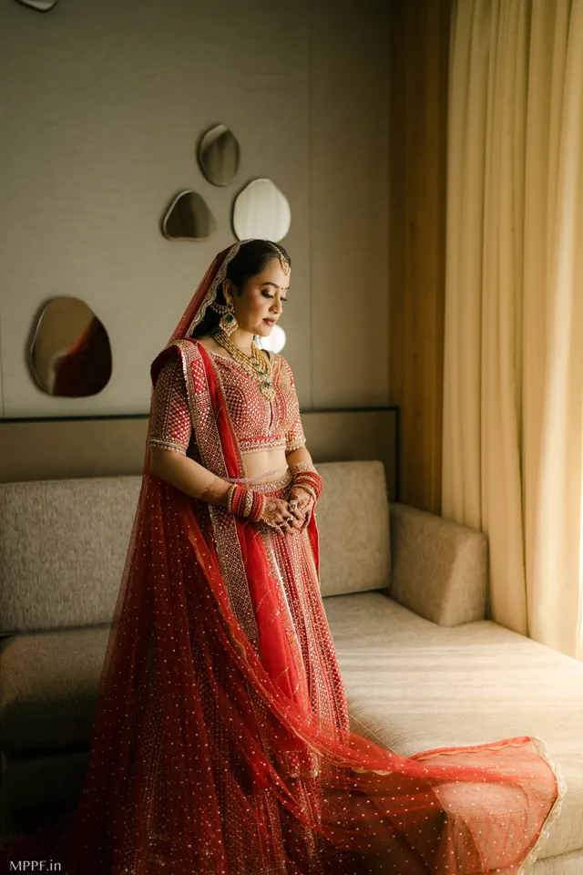 Bride in a red lehenga by a window